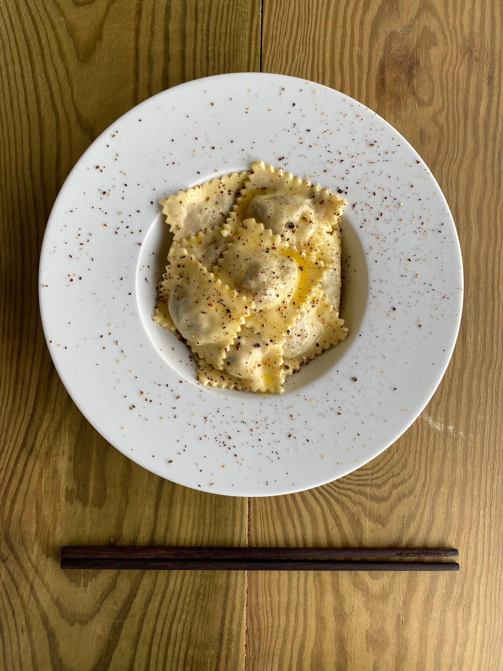 Assiette de raviolis vue de dessus, baguettes posées sur une table en bois.