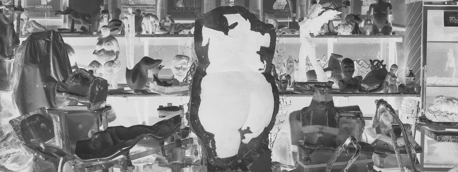 Torse sculpté au centre d'une vitrine chargée d'objets, en noir et blanc inversé.